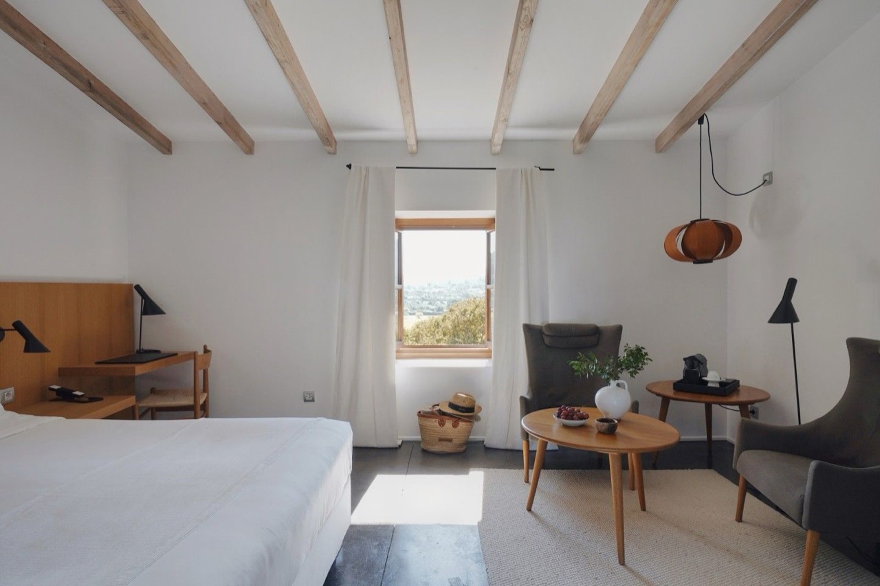 Guest room at Son Brull with wood beam ceiling, a bed, armchairs, and a window looking over the countryside