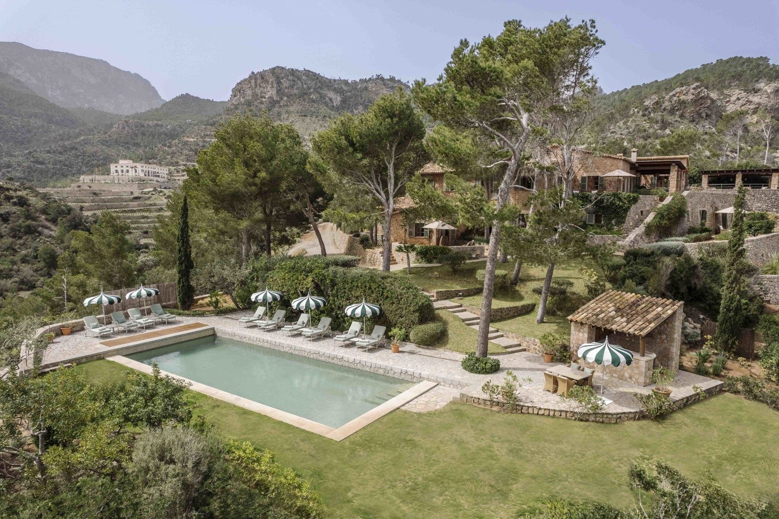 Aerial view of Sa Punta de S'Aguila, one of Son Bunyola's villas, with its own pool, striped umbrellas and stone farmhouse buildings among pine trees