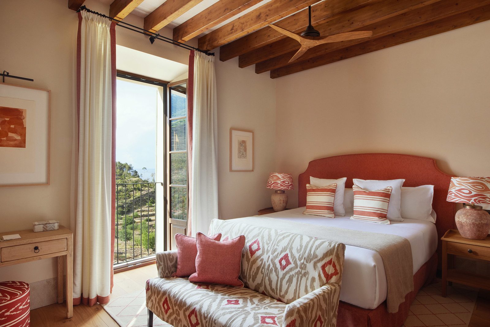 Sea View Room at Son Bunyola with a terracotta upholstered headboard, an ikat-patterned bench, a wood beam ceiling and French balcony doors open to a mountain and sea view