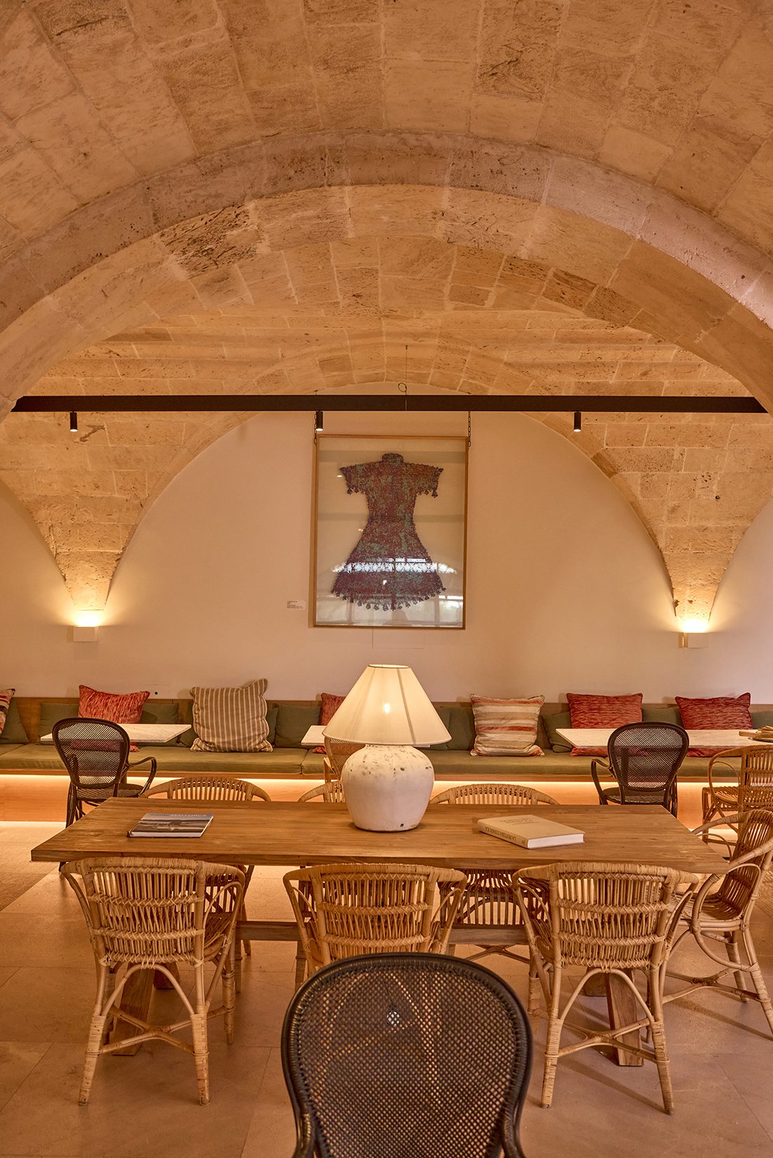 Vaulted stone dining room at Son Julia with rattan chairs around a wood table, a cushioned banquette and framed artwork on the wall