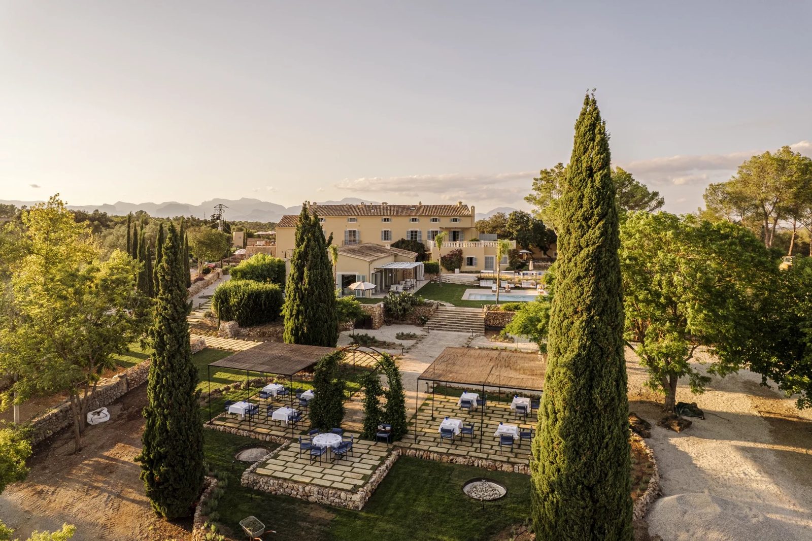 Aerial view of the pale yellow finca with cypress trees, terraced gardens, outdoor dining tables and the pool