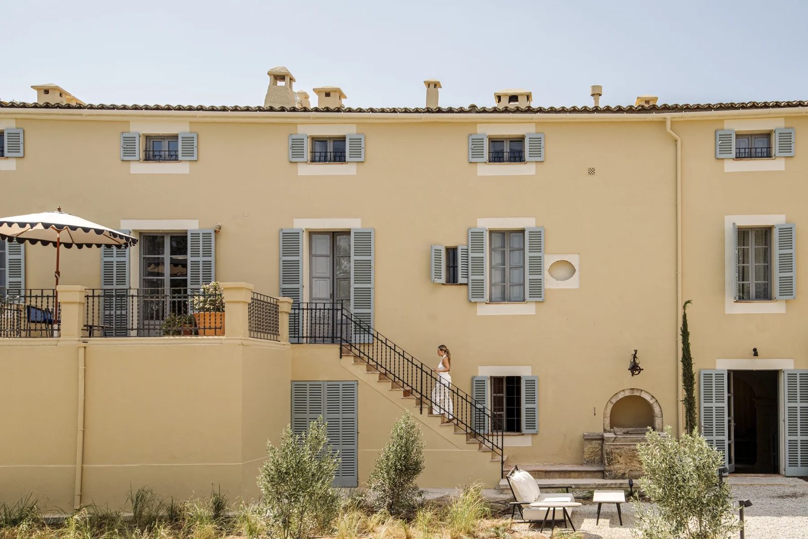 Yellow finca facade with grey-blue shutters, a terrace and an outdoor stone staircase