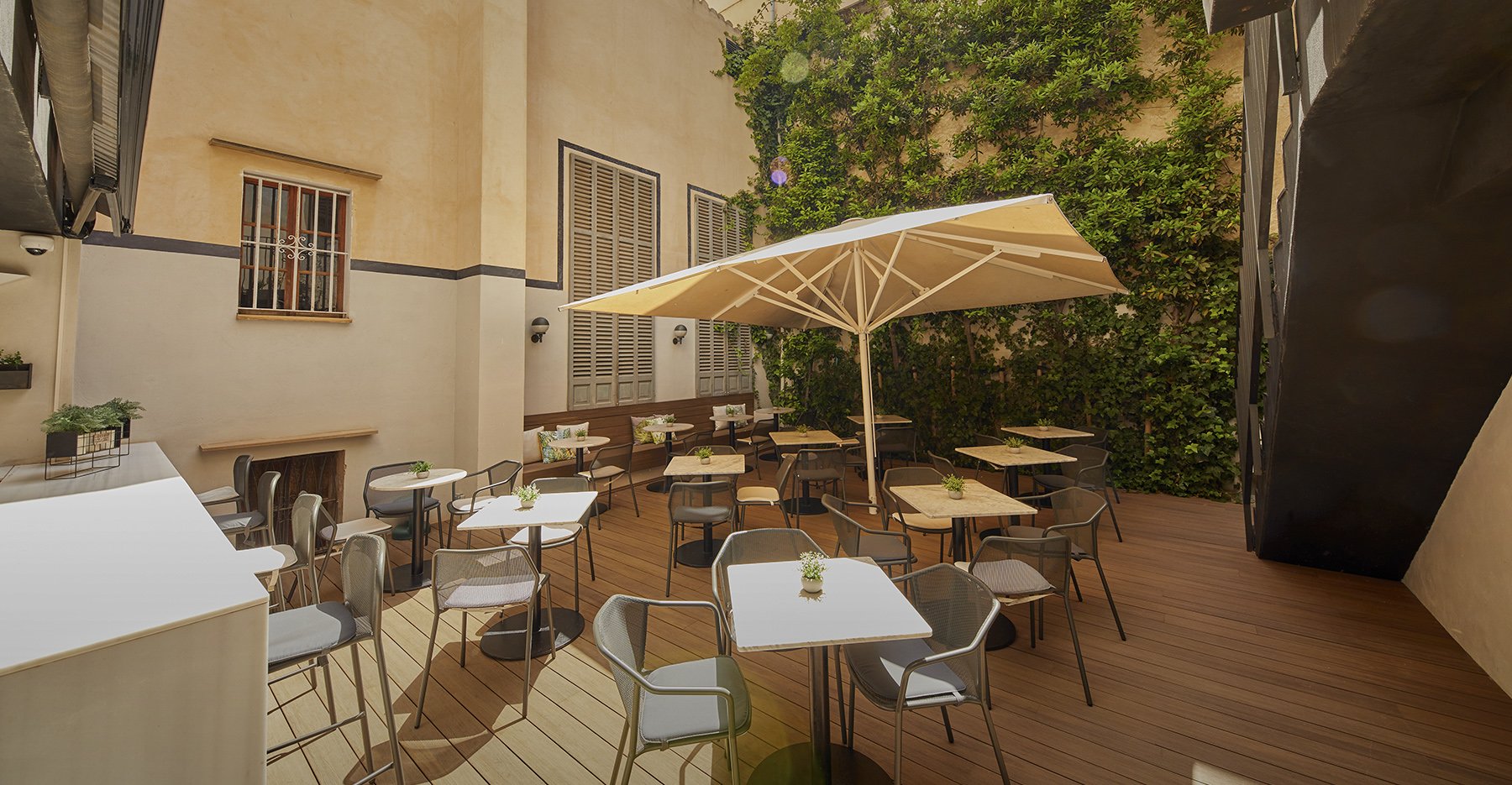 Courtyard terrace with tables and a parasol beside a climbing-plant wall