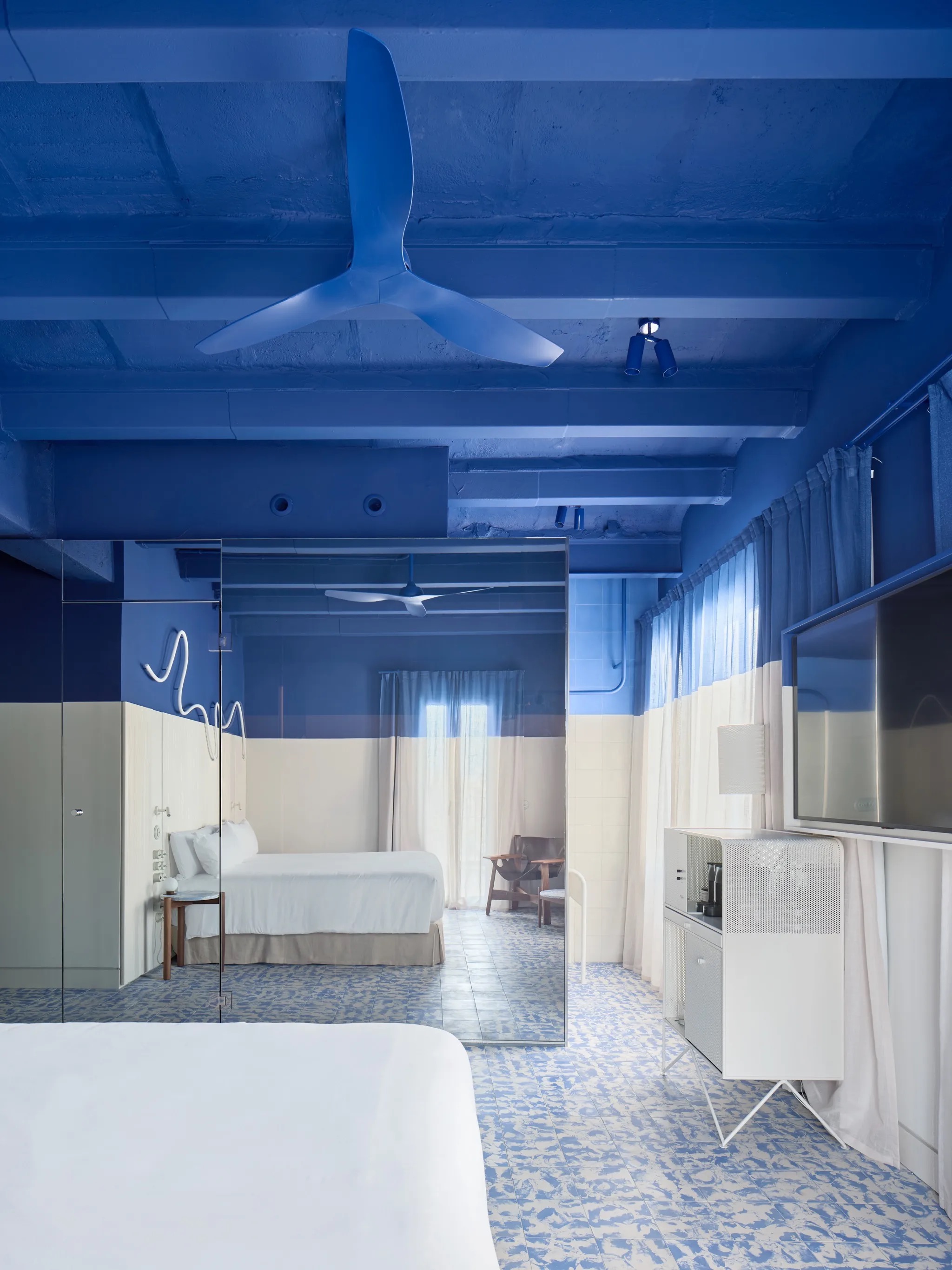 Blue-toned guest room with a mirrored wardrobe, patterned tile floor, and a wall-mounted flat-screen TV