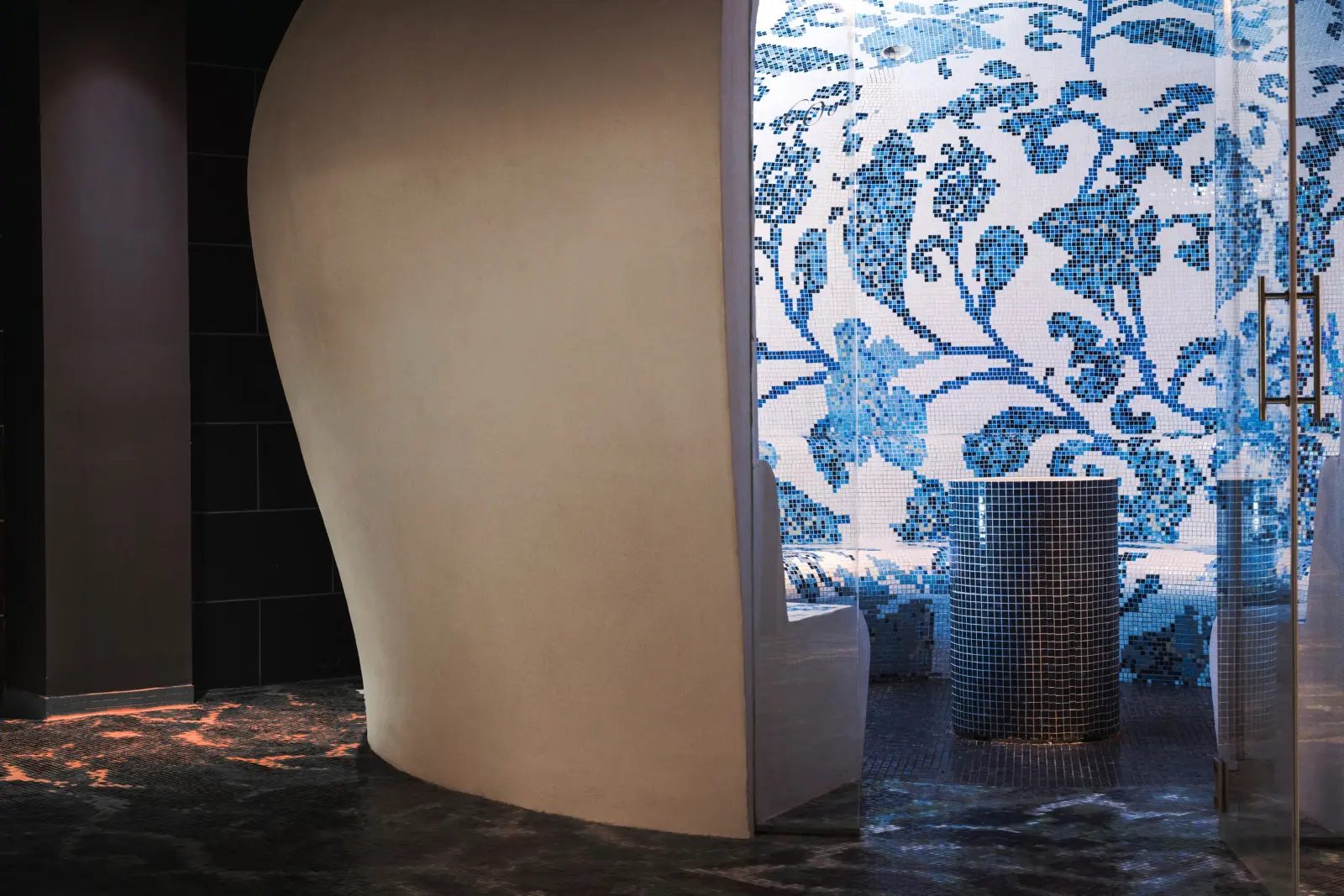 Spa steam room at The Donna Portals with an intricate blue floral mosaic tile wall, a curved sculptural partition and a glass door