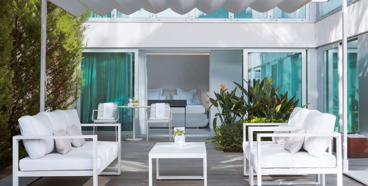 Private terrace at The Donna Portals with white outdoor sofas and a coffee table beside a ground-floor room visible through glass doors with teal curtains