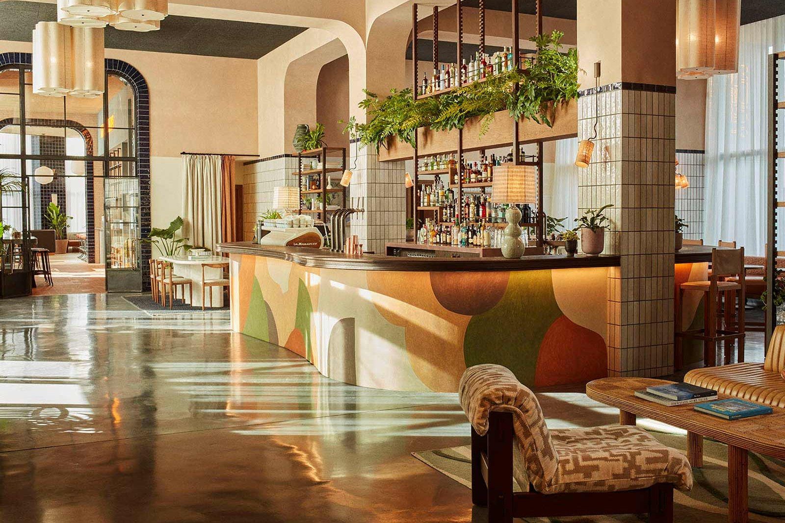Lobby bar at The Hoxton Poblenou with a curved colour-blocked terrazzo-style bar front, hanging plants and a patterned tile column