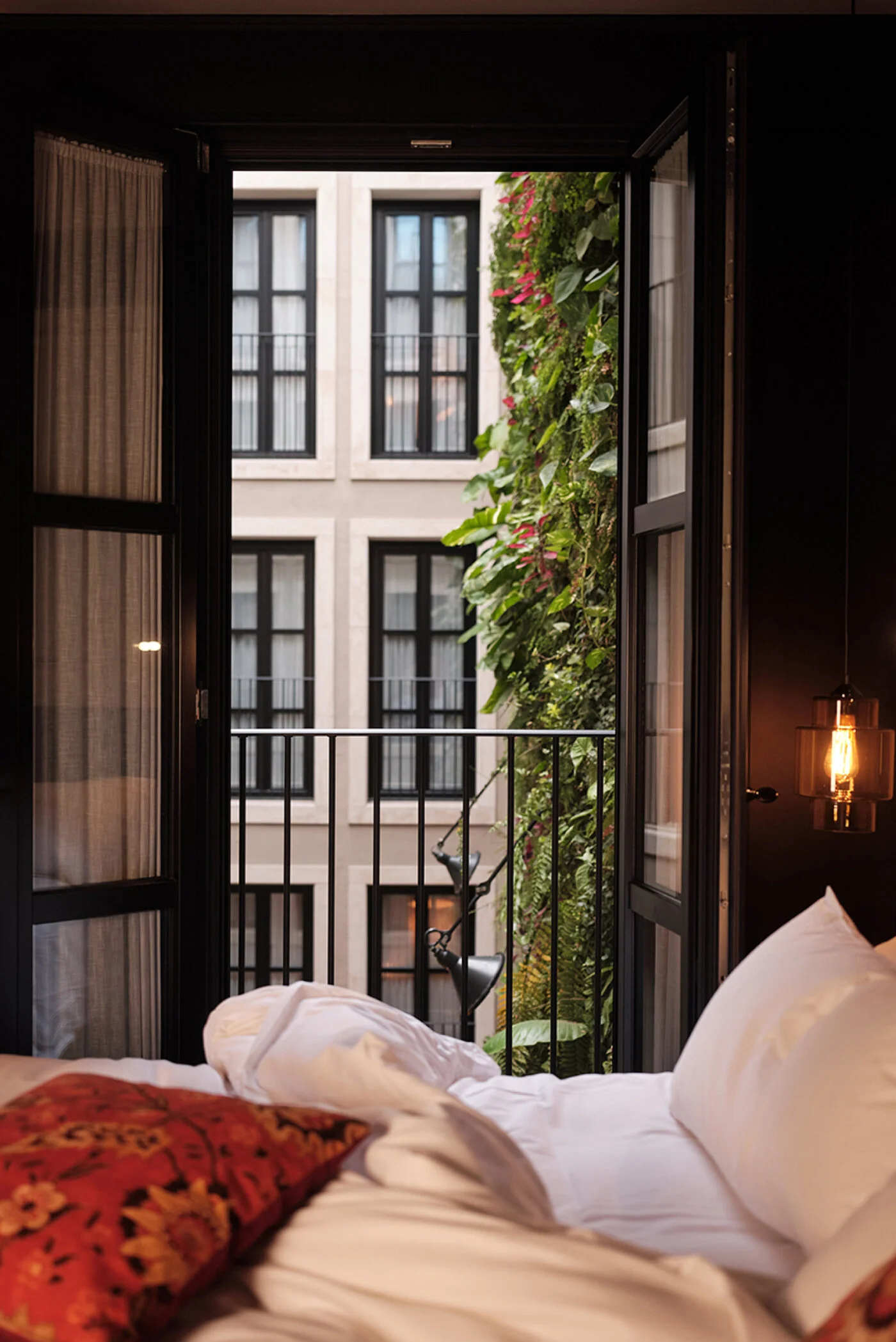 Guest room with an open balcony door overlooking a plant-covered courtyard facade