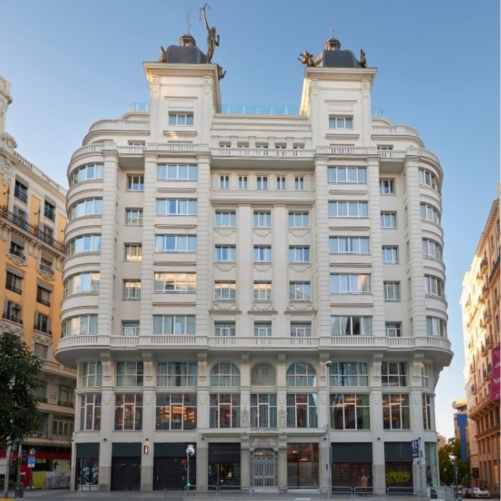 The hotel's white stone facade with rounded corner balconies, topped by sculptures, against a blue sky.