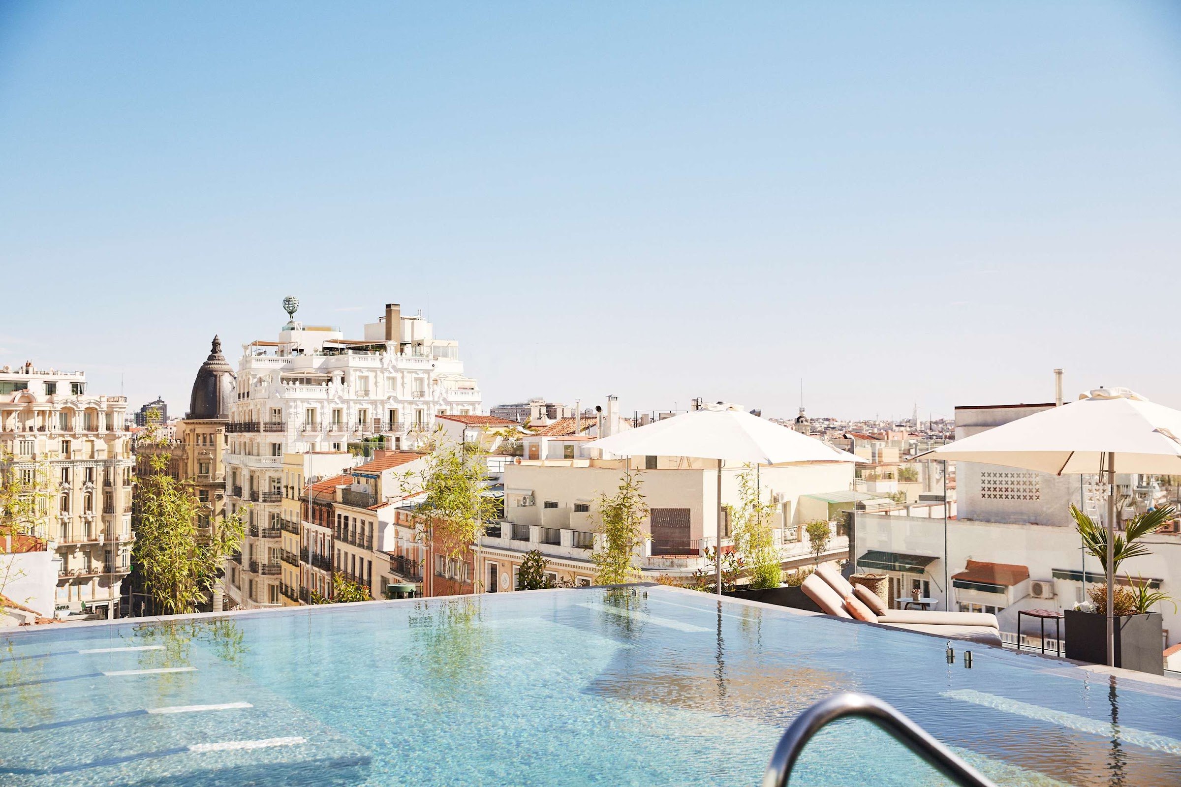A rooftop infinity pool with white parasols and loungers, its edge running out towards the rooftops of central Madrid.