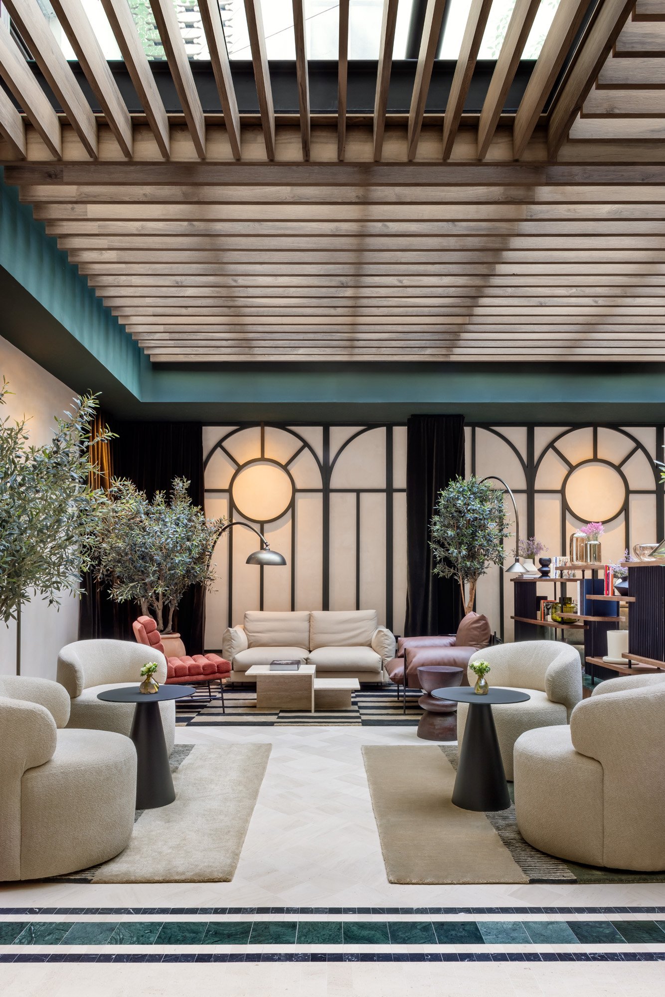 A lounge area with cream armchairs and sofas, a slatted wooden ceiling with a skylight and a green tiled floor border.