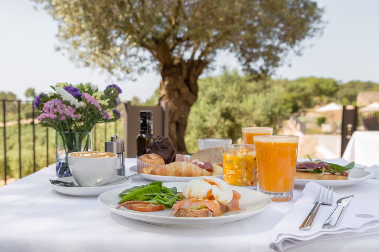 Breakfast spread on a terrace table at Treurer, with pastries, juice, and eggs under an olive tree