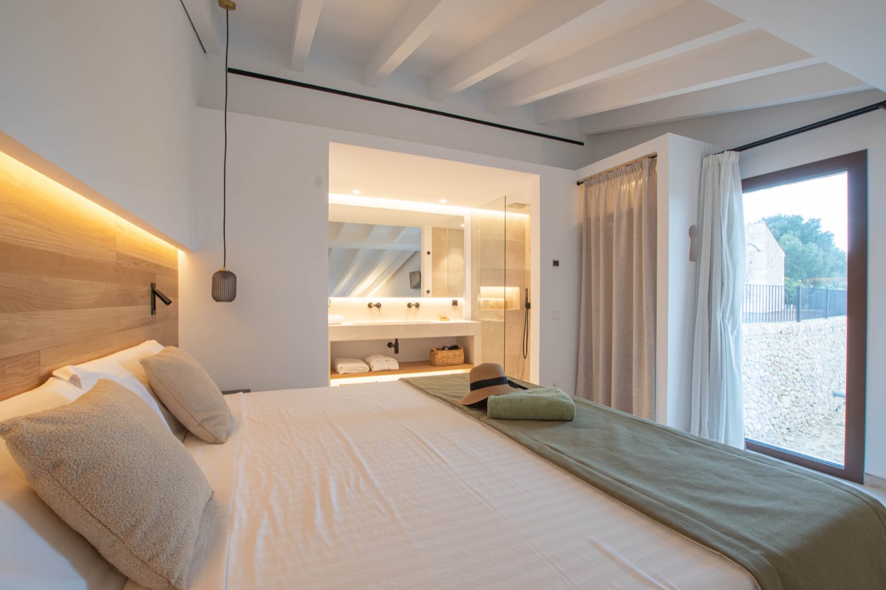 Bedroom suite at Treurer with a bed, open ensuite bathroom, and a window looking over the stone wall outside