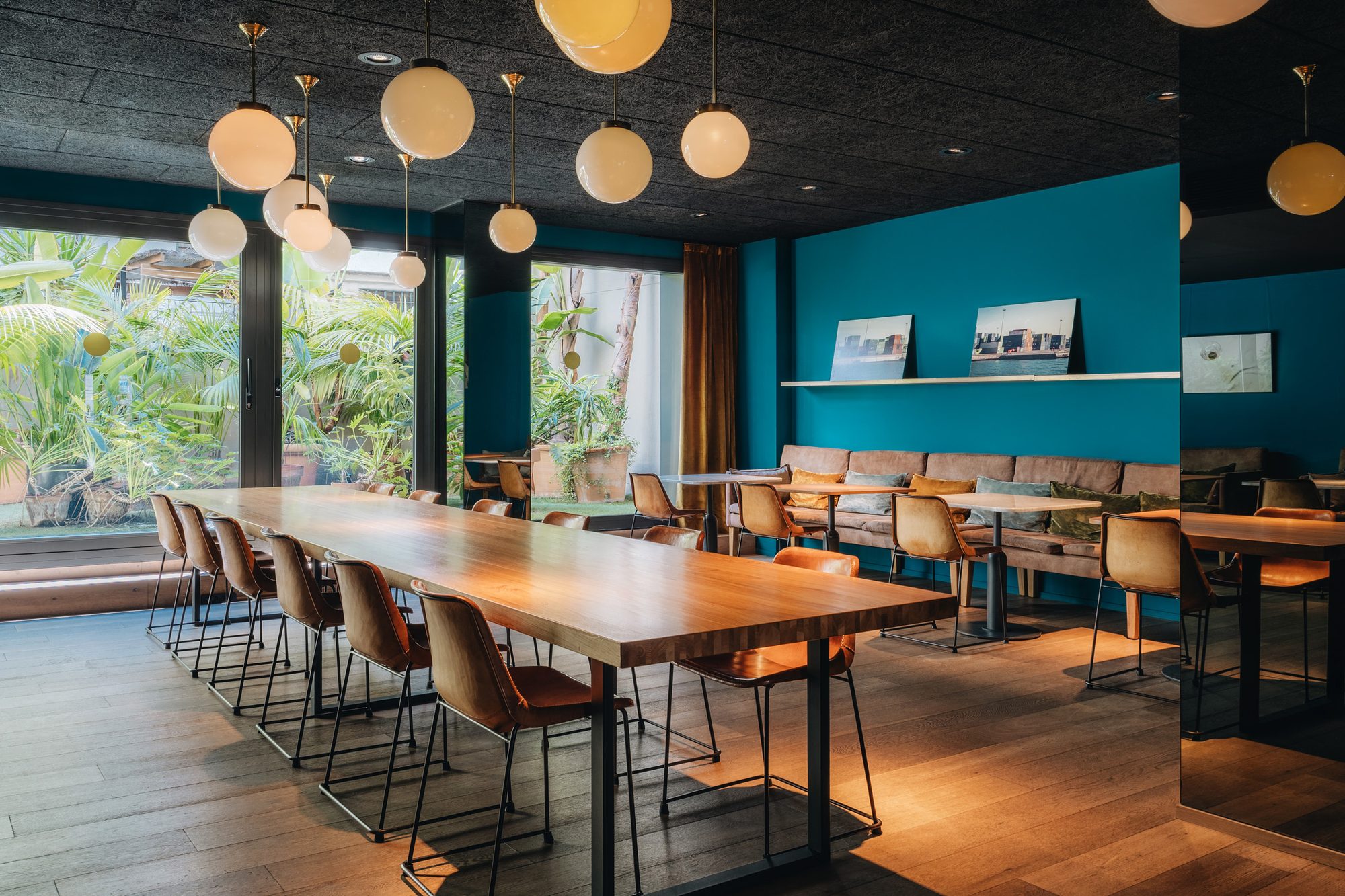 Dining room at Uma House by Yurbban with a long communal wood table, tan leather chairs, globe pendant lights and a teal banquette along the wall