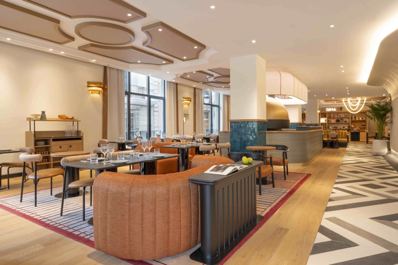 The GINA restaurant dining room, with orange banquette seating, wood floors, a tiled pizza oven and a lit GINA sign at the back.