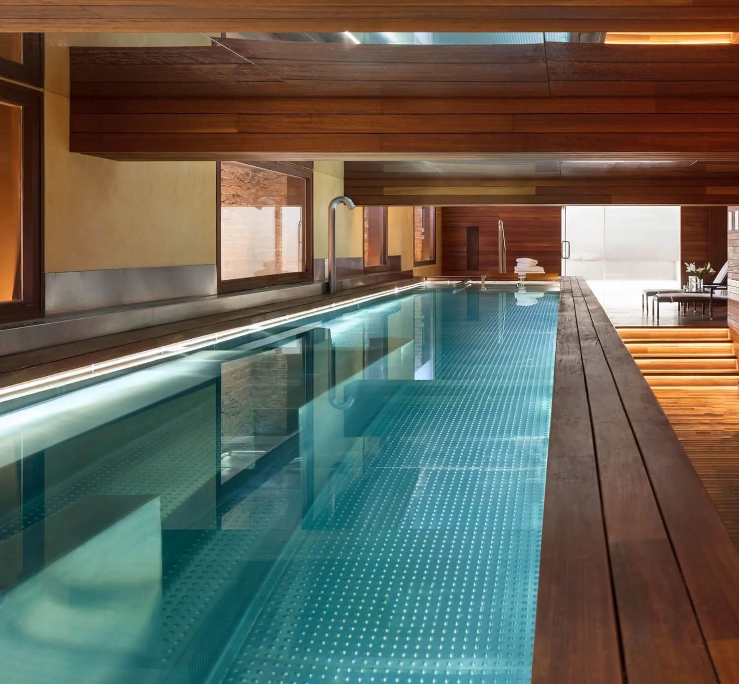 An indoor lap pool lined in dark timber, with lit strips running along the water's edge and loungers on the decking at the far end.