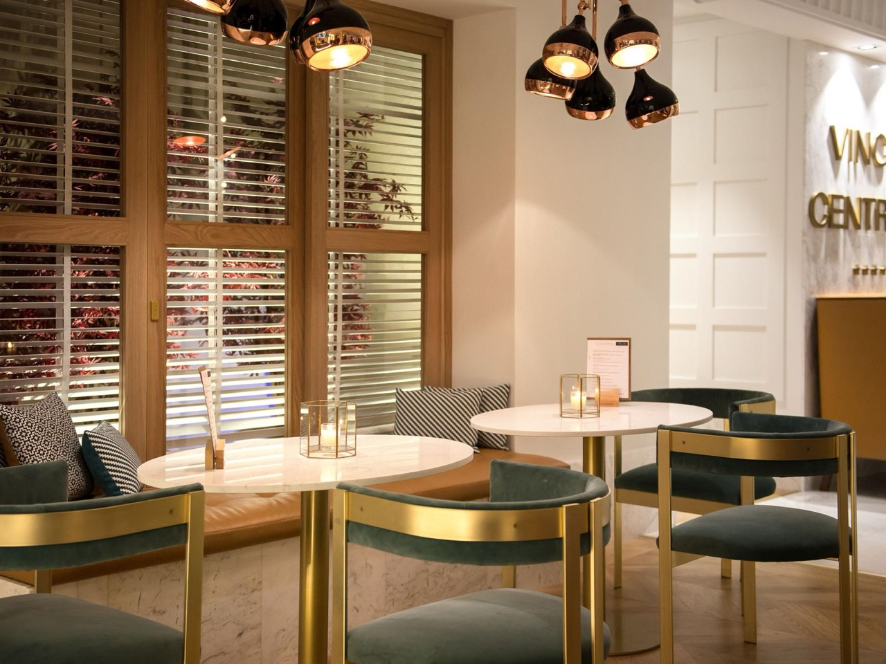 Hall Lounge seating area with round marble tables, green velvet and brass chairs, and a cocktail menu card on the table, near the Vincci Centrum sign.