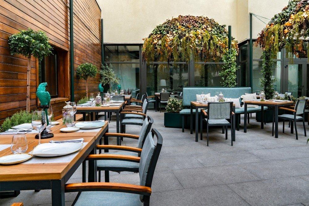 Vincci Soho's covered courtyard terrace with wooden dining tables, teal chairs and potted plants against a wood-panelled wall.