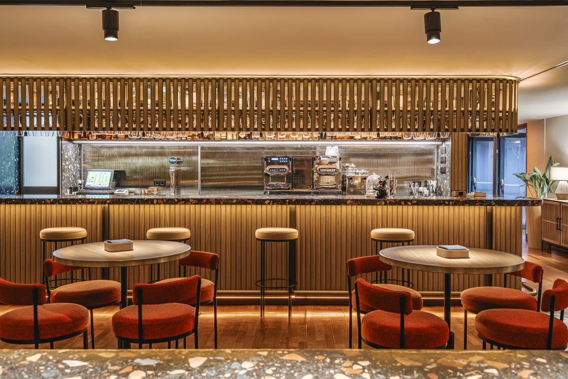 The SoMa Bar counter with fluted wood panelling, hanging wine glasses and round tables with rust-colored upholstered chairs.