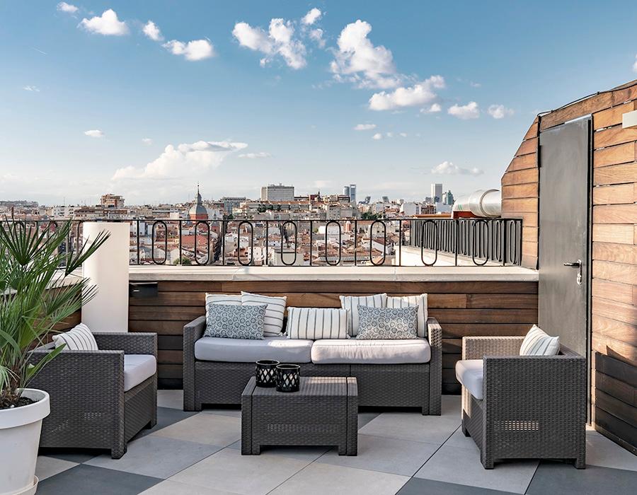 The rooftop terrace with wicker sofas and armchairs, a low table and potted plants, overlooking Madrid's rooftops and skyline.
