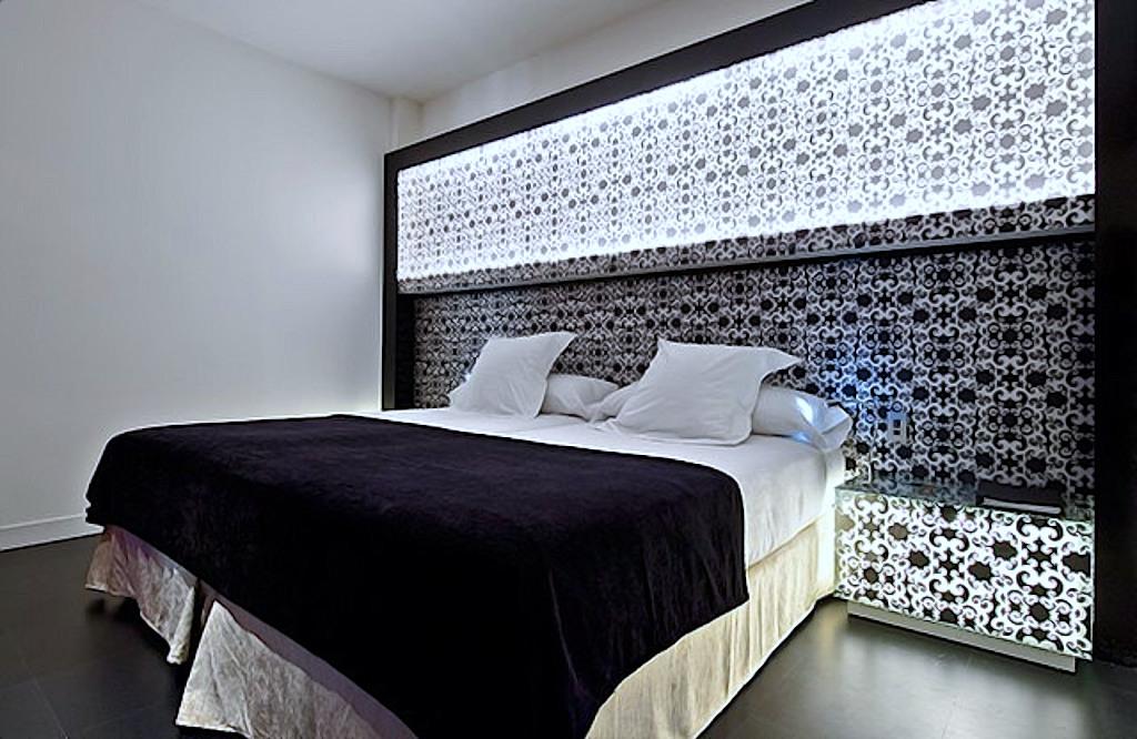 A hotel double bed with a black and white patterned illuminated headboard and dark velvet bedspread.