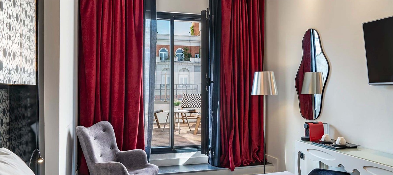 A room's private terrace seen through an open door, with outdoor seating and a small table against a city view.