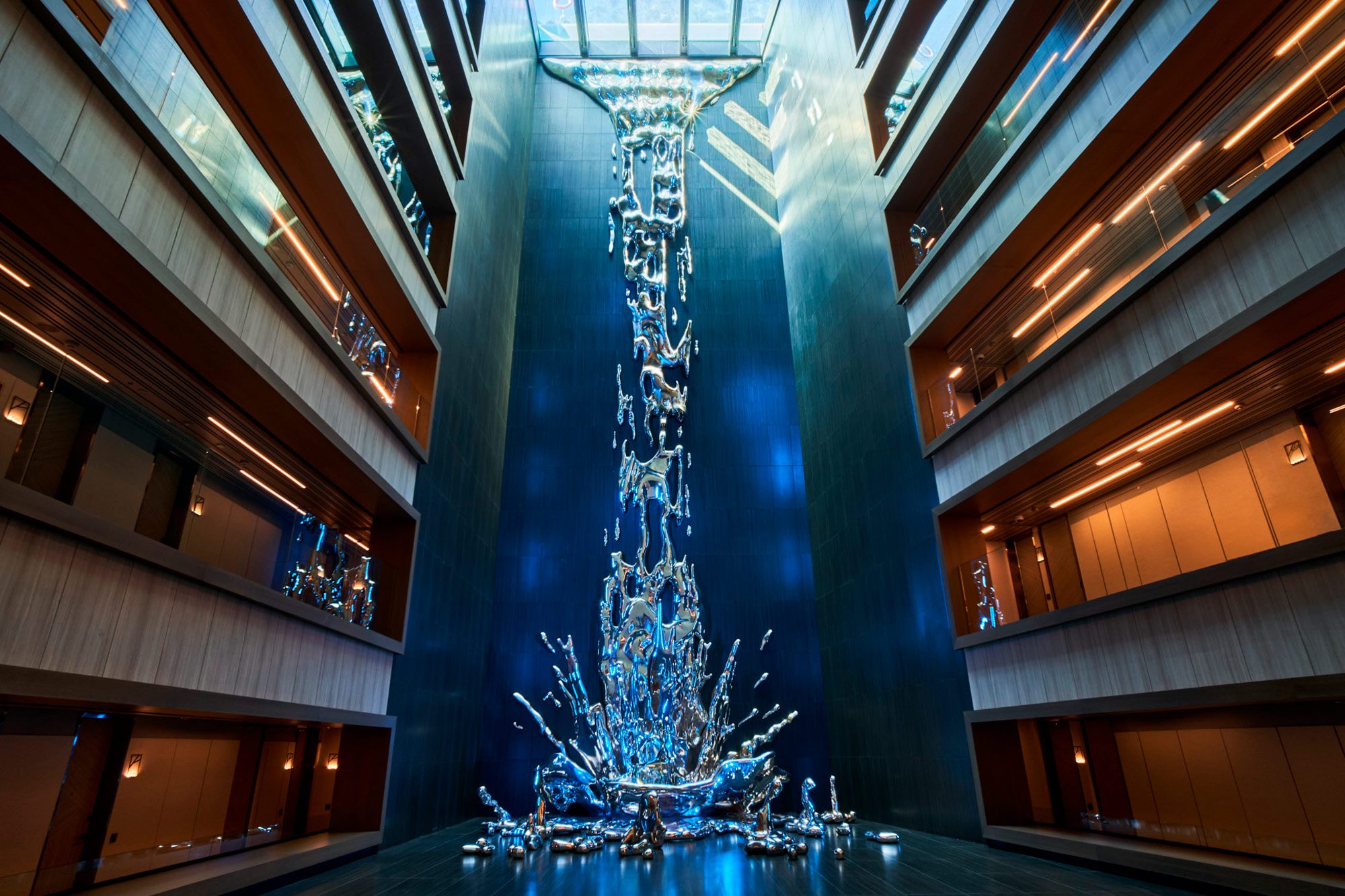 The hotel's atrium, where a mirrored sculpture of falling and splashing water runs down a blue-lit wall between balconied corridors on both sides.