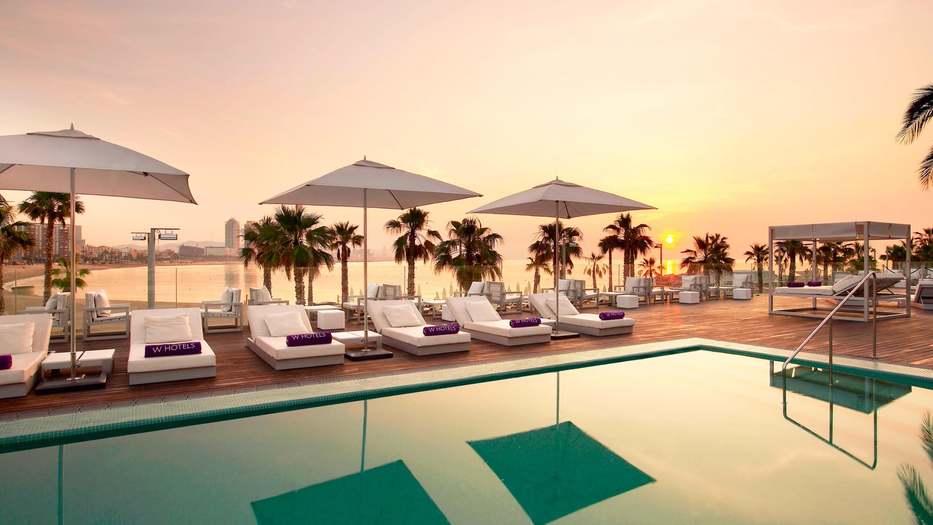 Rooftop pool deck at sunset with branded loungers and a sea view