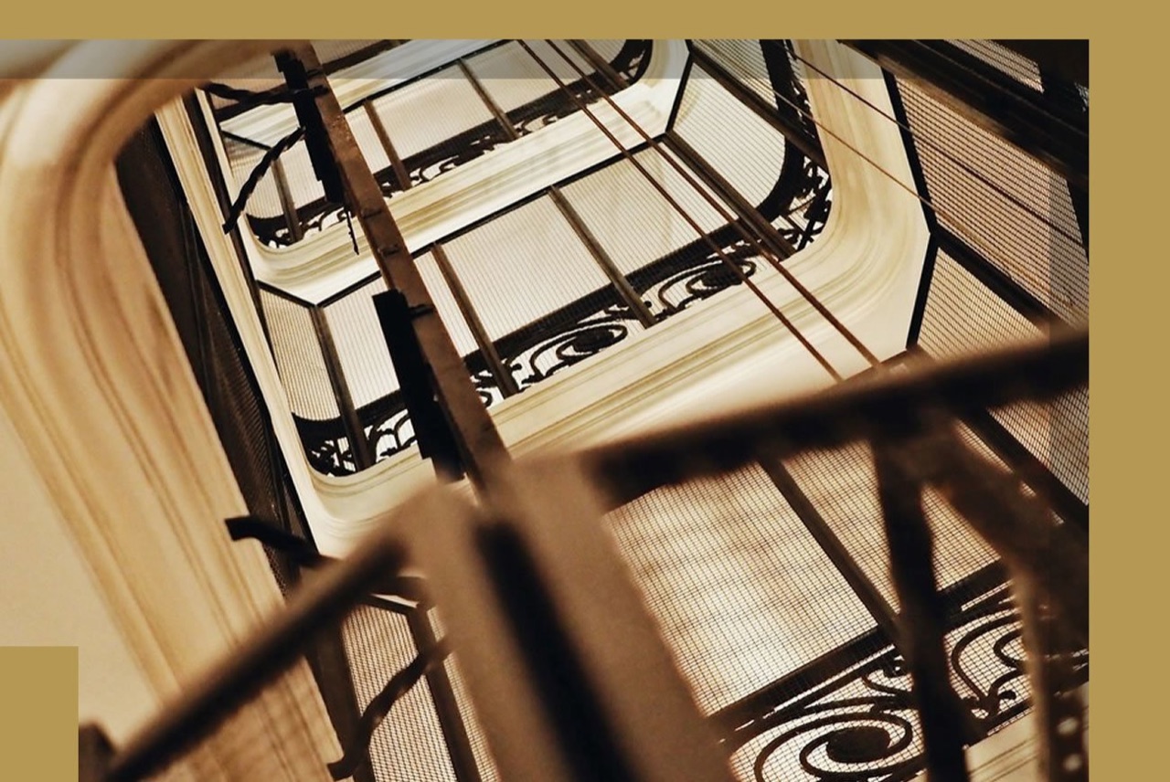 A view looking up an ornate wrought-iron stairwell shaft with skylights at the top of the building.