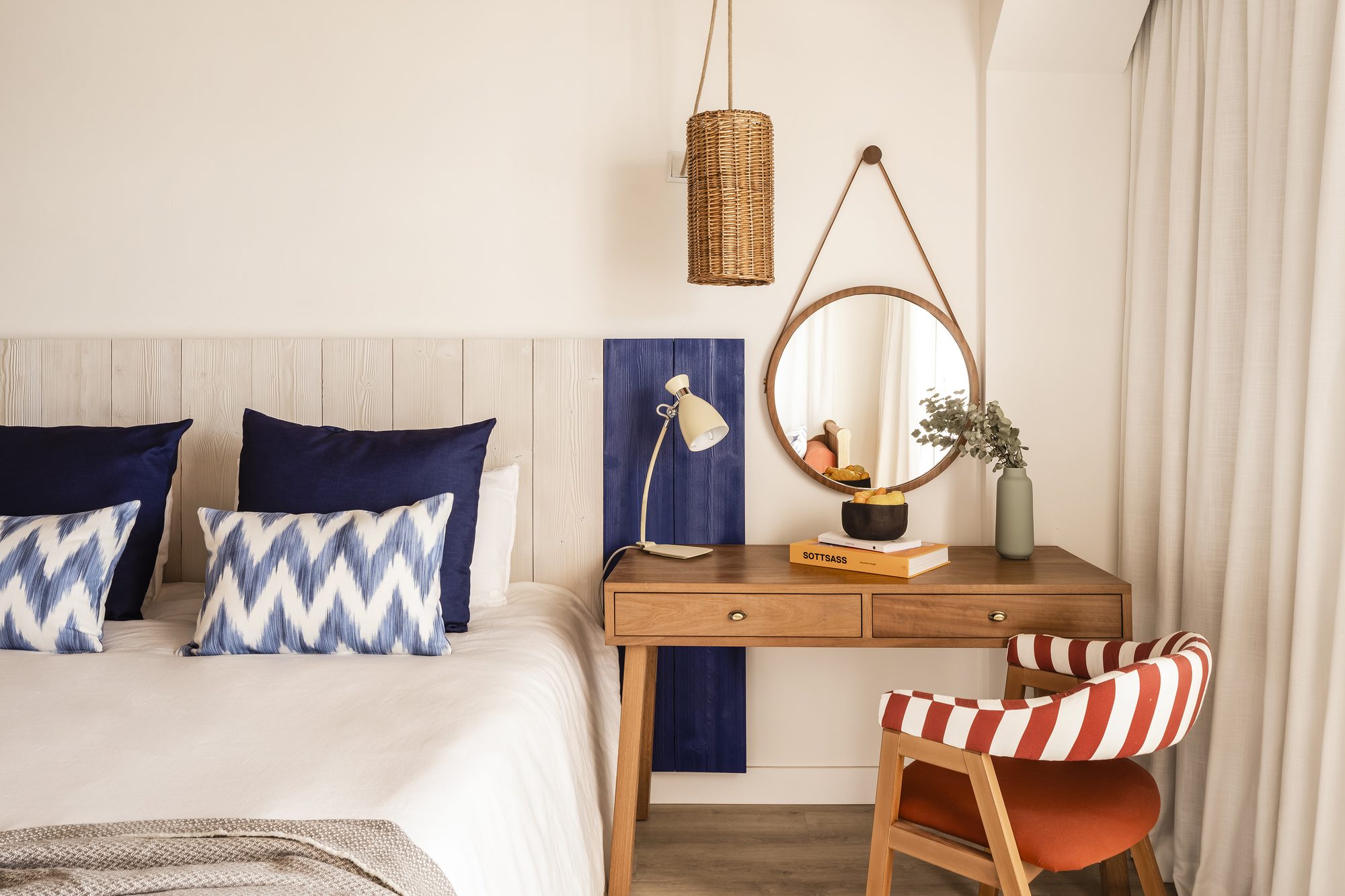 Guest room at Zel Mallorca with a whitewashed slat headboard, navy and chevron-patterned pillows, and a round wood-framed mirror over a wooden desk
