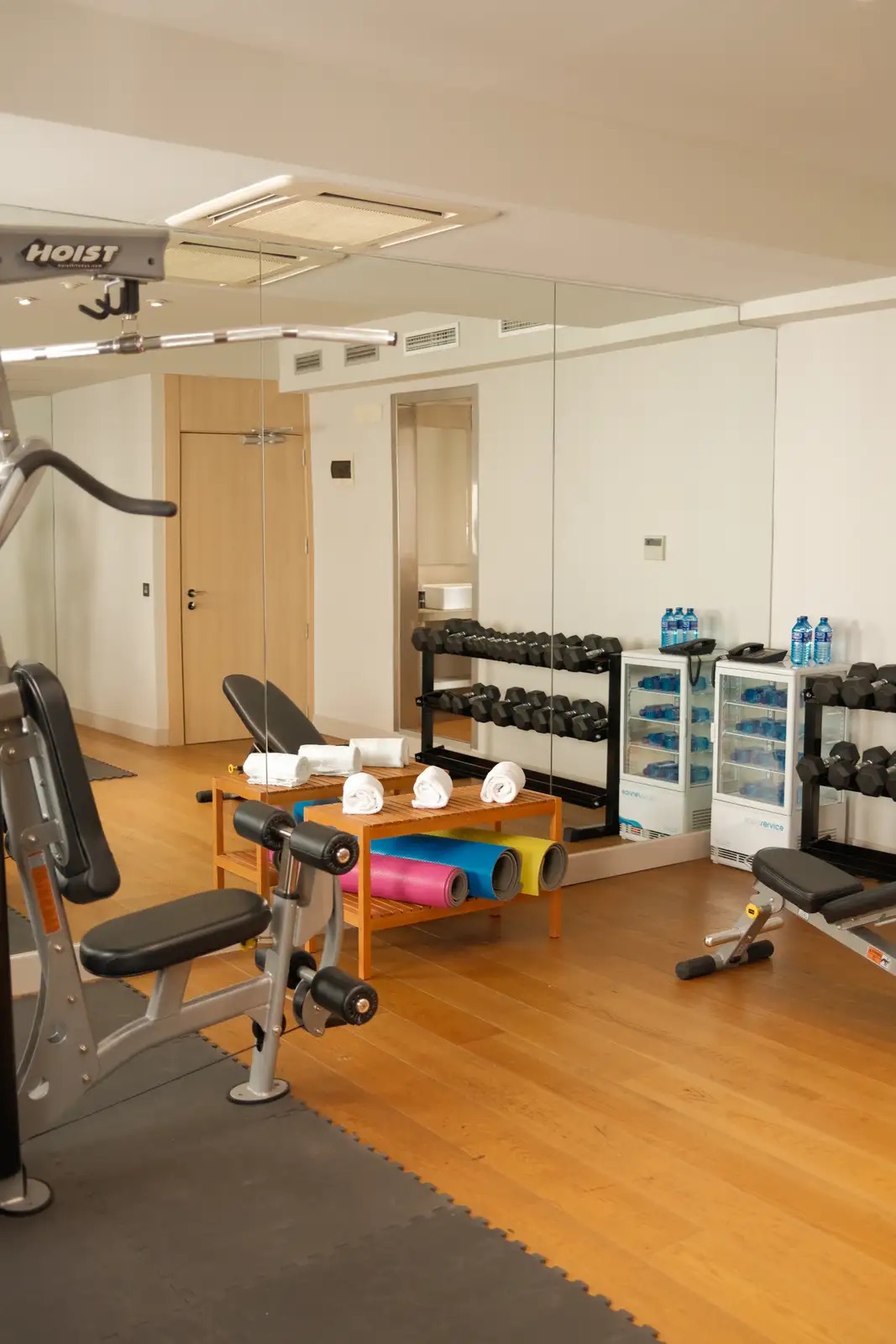 The hotel gym with weight machines, a dumbbell rack, rolled exercise mats and bottled water in display fridges.