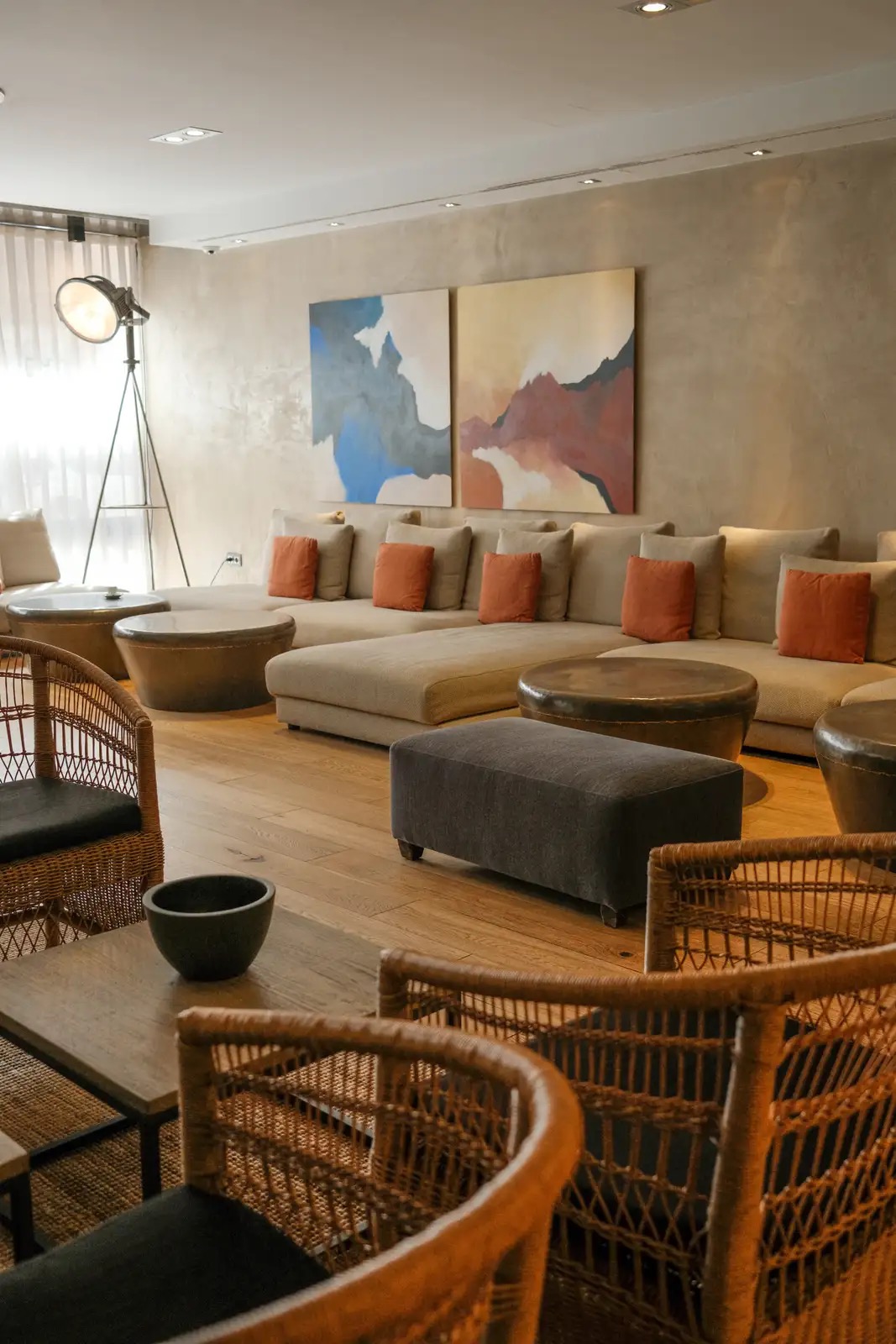 A lounge seating area with a beige sectional sofa, orange cushions, wicker armchairs and abstract wall art.