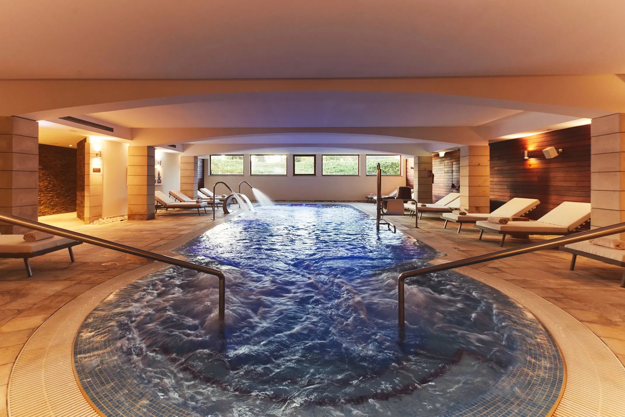 Indoor spa pool with a whirlpool jet feature, stone tile surround, and rows of loungers