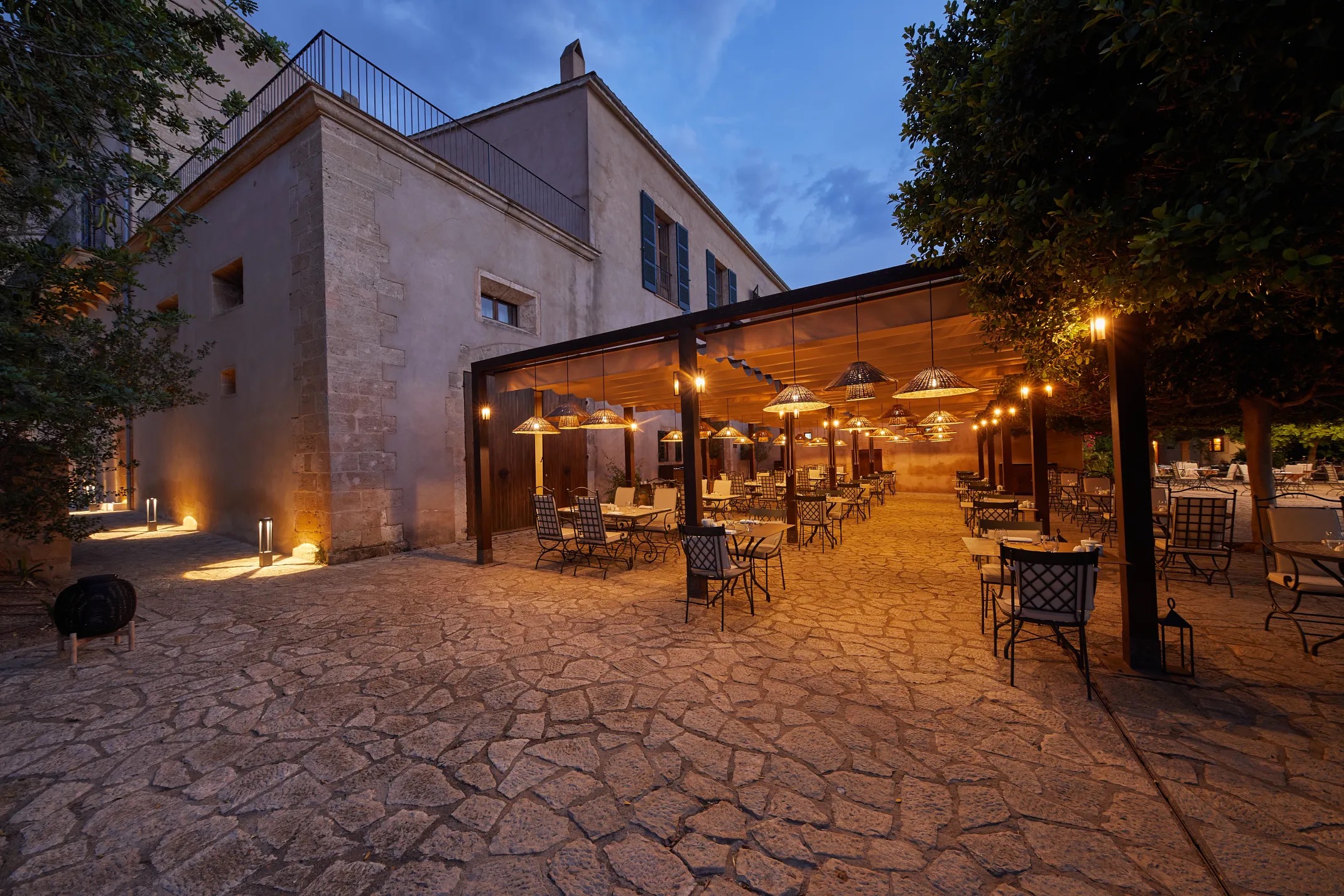 Es Mercat restaurant's covered outdoor terrace set for dinner service at dusk, string of pendant lamps overhead
