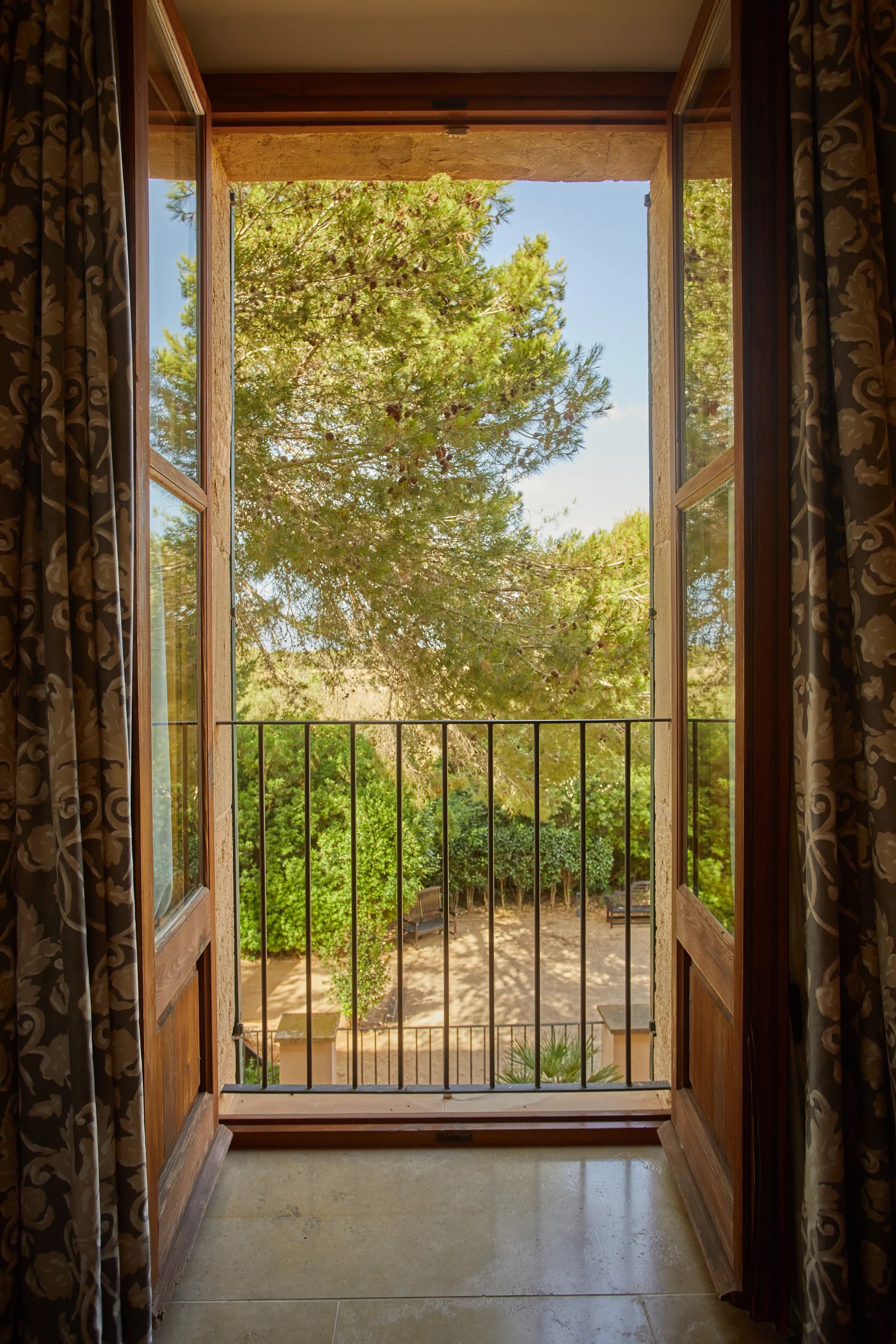 View from an open guest-room balcony door across a pine tree and garden terrace below
