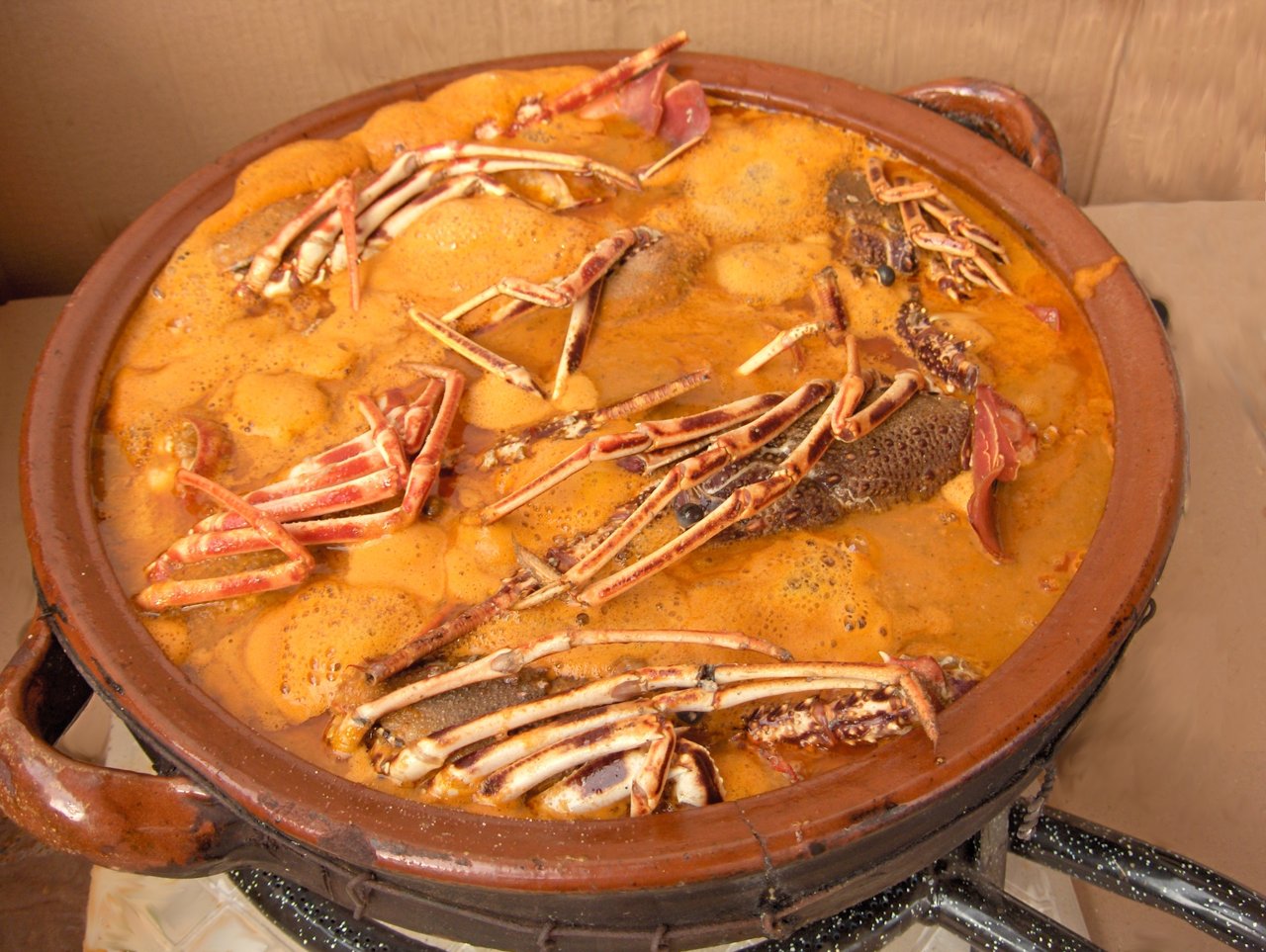 A clay cazuela of caldereta de llagosta, a Menorcan lobster stew, with crab and lobster legs in an orange saffron broth