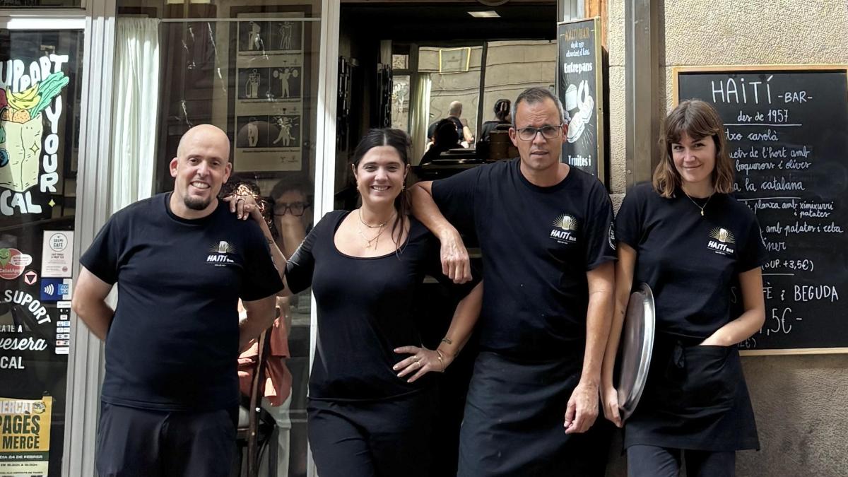 Four staff members in black Haití Bar T-shirts standing outside the bar's entrance, with a chalkboard menu reading 'HAITÍ BAR des de 1957' beside them