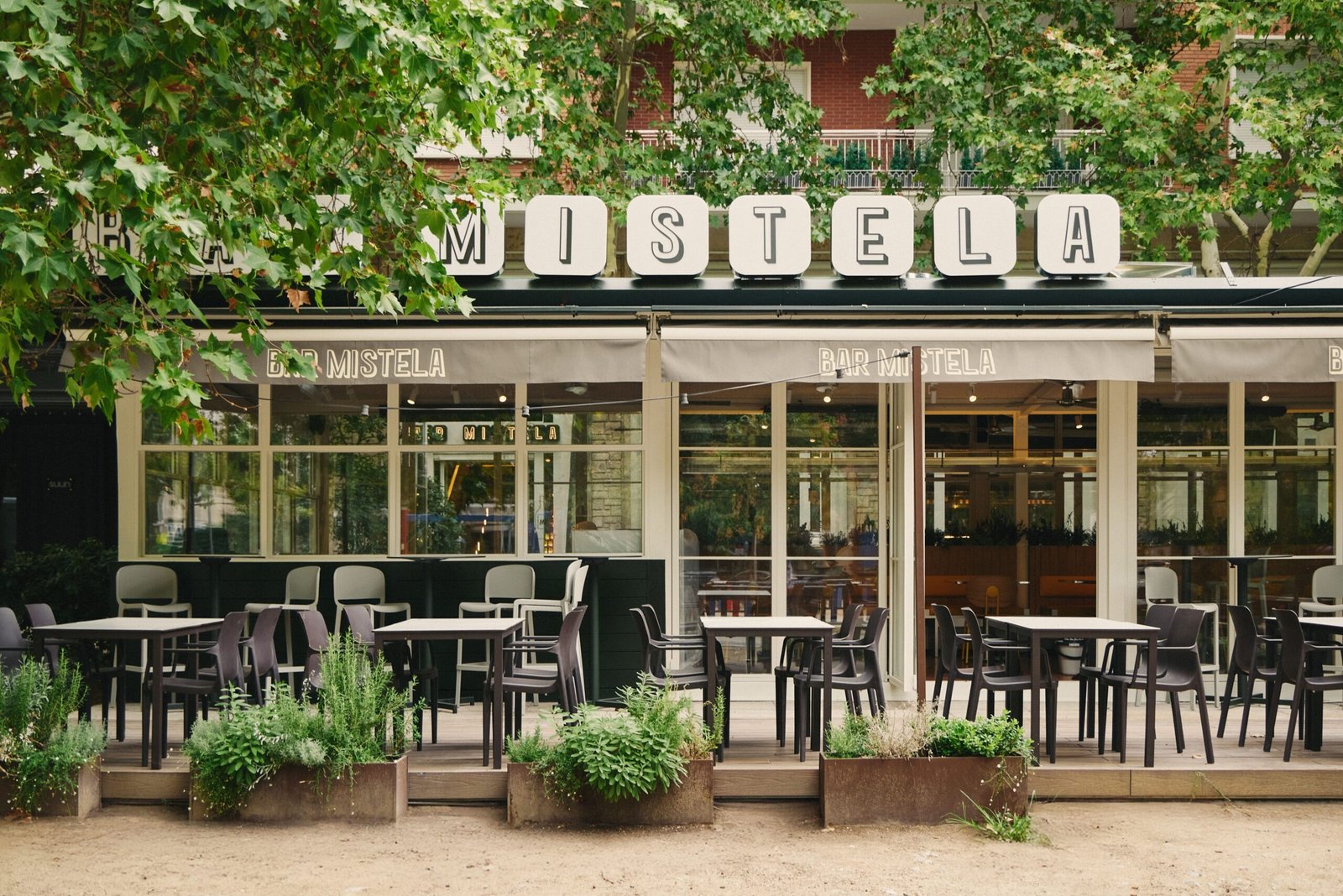 The Bar Mistela frontage with its sign and terrace tables under trees.