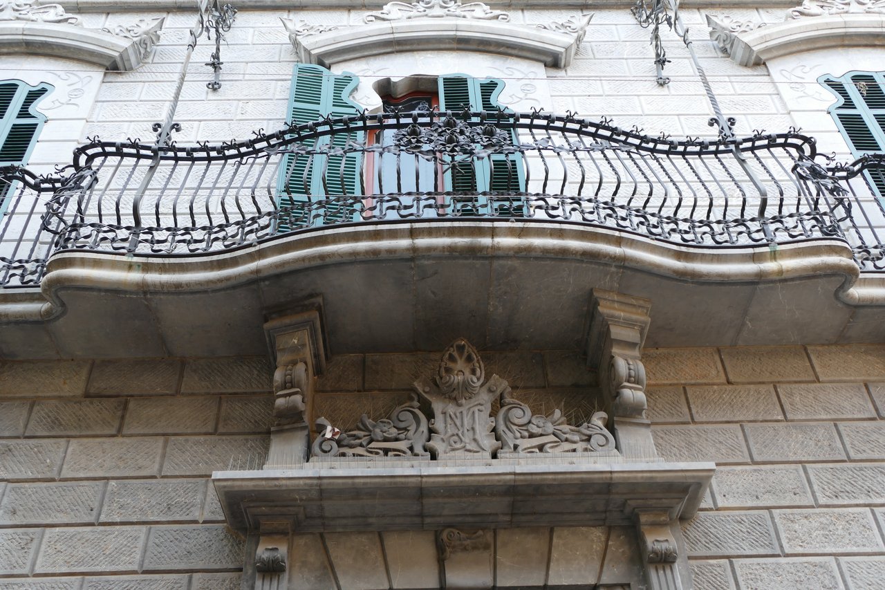 Ornate wrought-iron modernist balcony with turquoise shutters on the carved stone facade of Can Prunera in Sóller