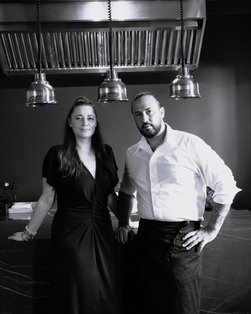 Black and white portrait of Marion and Javier, the couple behind Osma – Table Française in Palma, standing in their kitchen (not a photo of the wider Cuines del Món event)