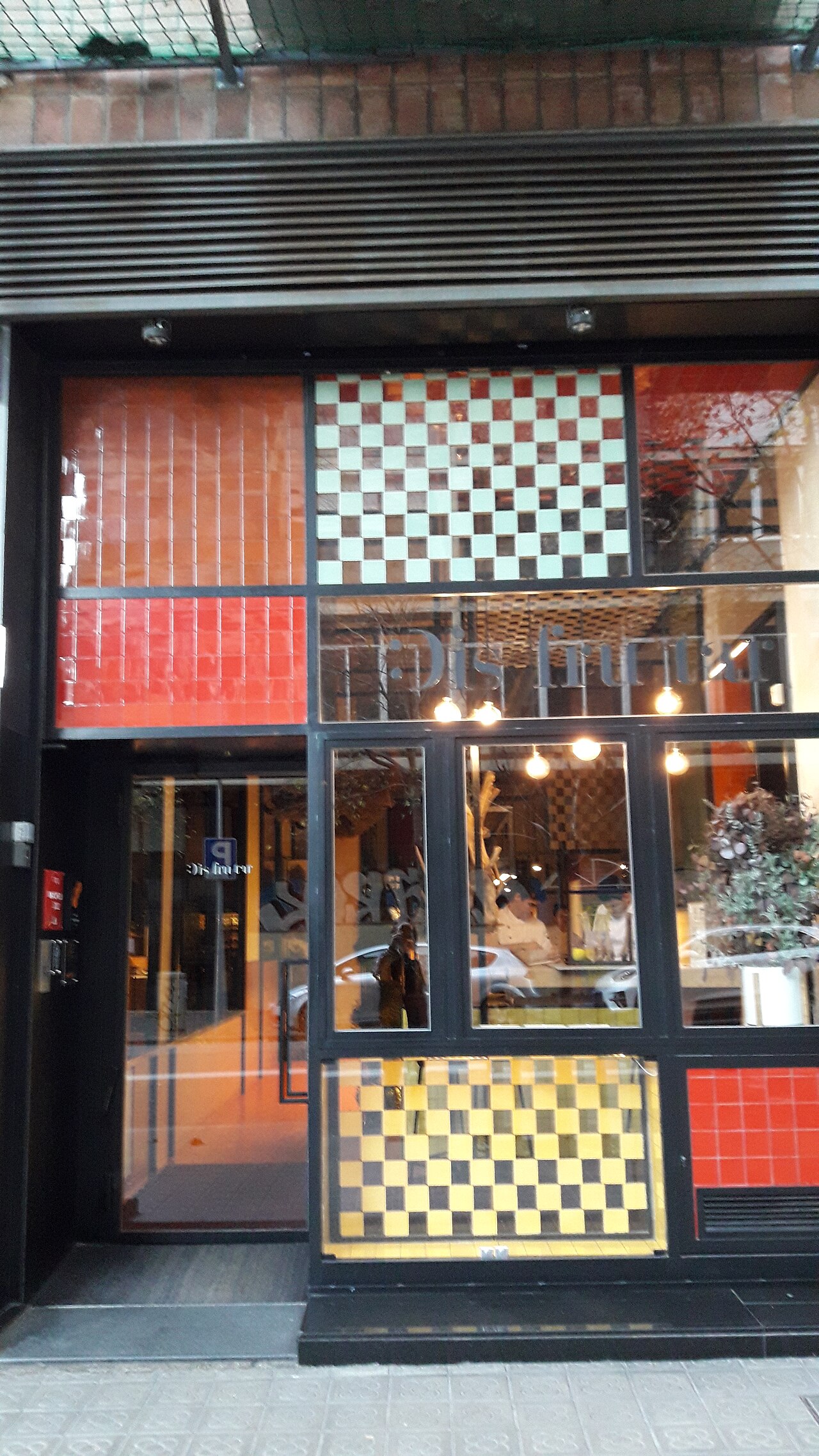The tile-clad street facade of Disfrutar restaurant on Carrer de Villarroel in Barcelona's Eixample, with the restaurant name etched on the window.