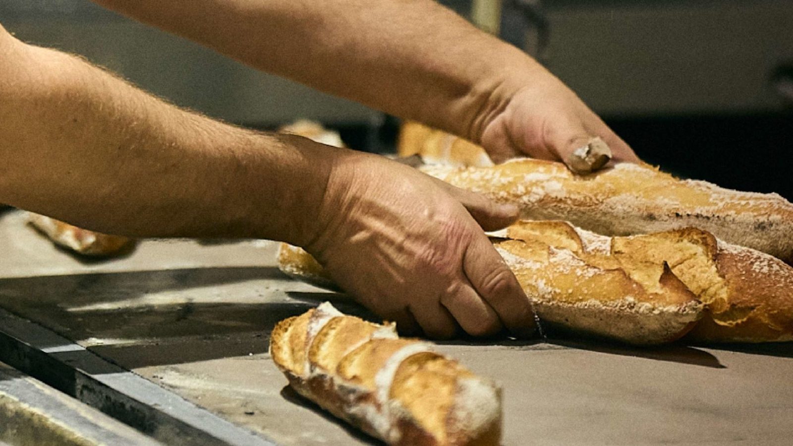 A baker's hands handling freshly baked baguettes at Forn Gil.