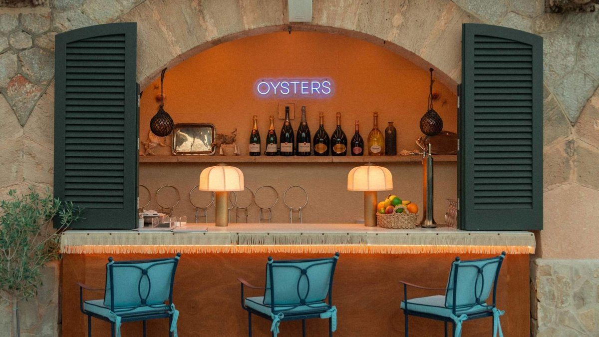 The Oyster Bar at Hospes Maricel: an arched stone counter with a neon 'Oysters' sign, champagne bottles and blue bar stools