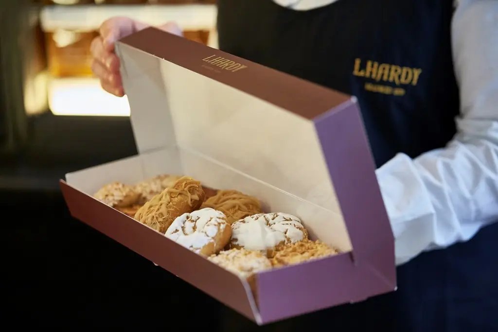 A staff member holding an open Lhardy box of glazed and iced pastries.