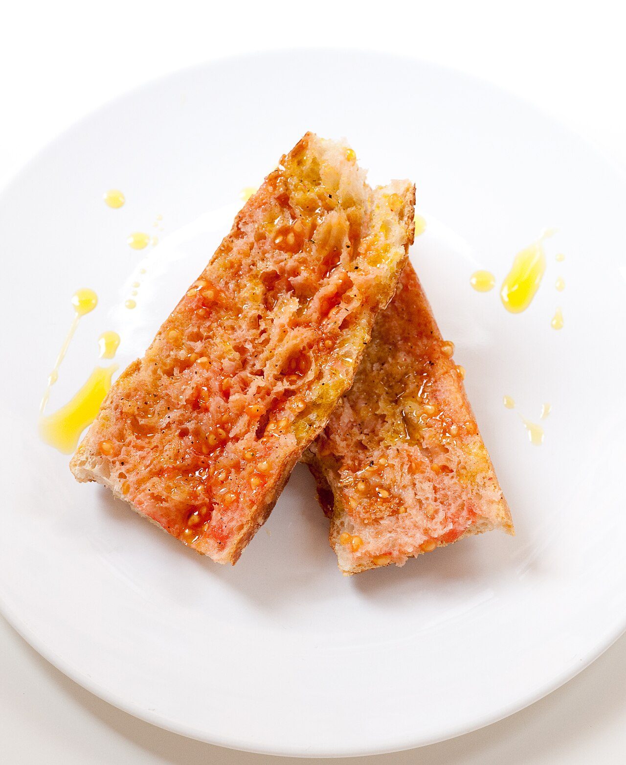 Two slices of pa amb tomàquet drizzled with olive oil on a white plate (illustrative, not PAMB)