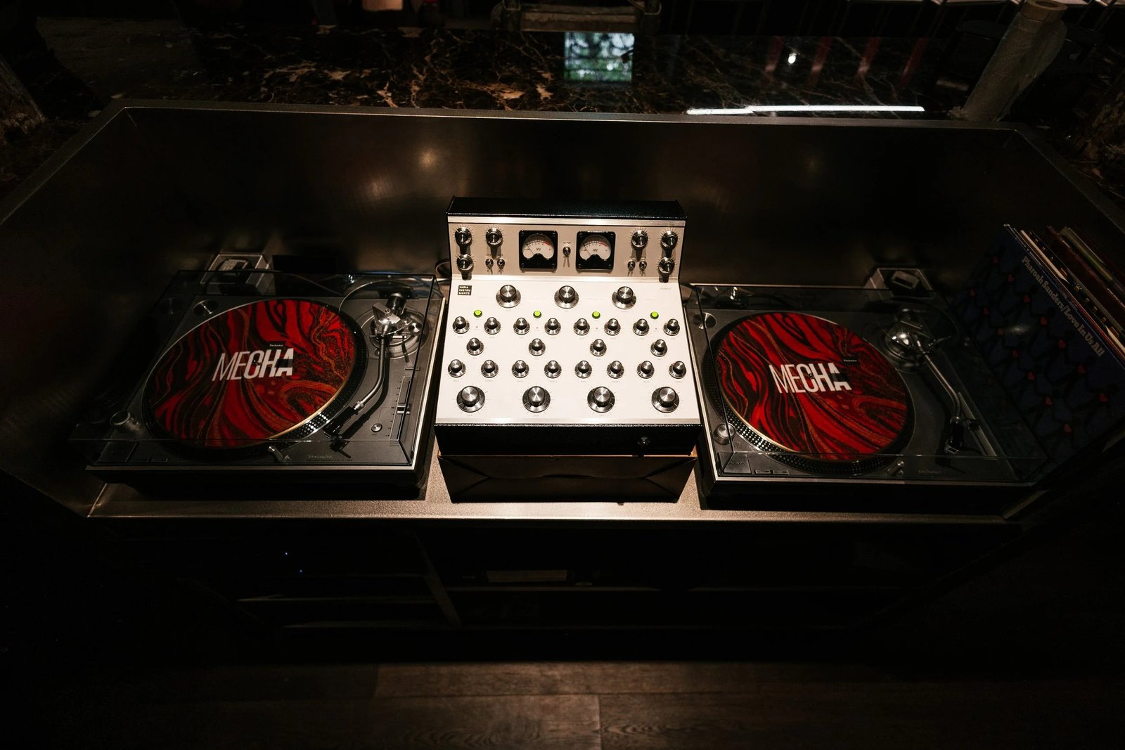 Two turntables and a mixer on a DJ booth in a dimly lit room.