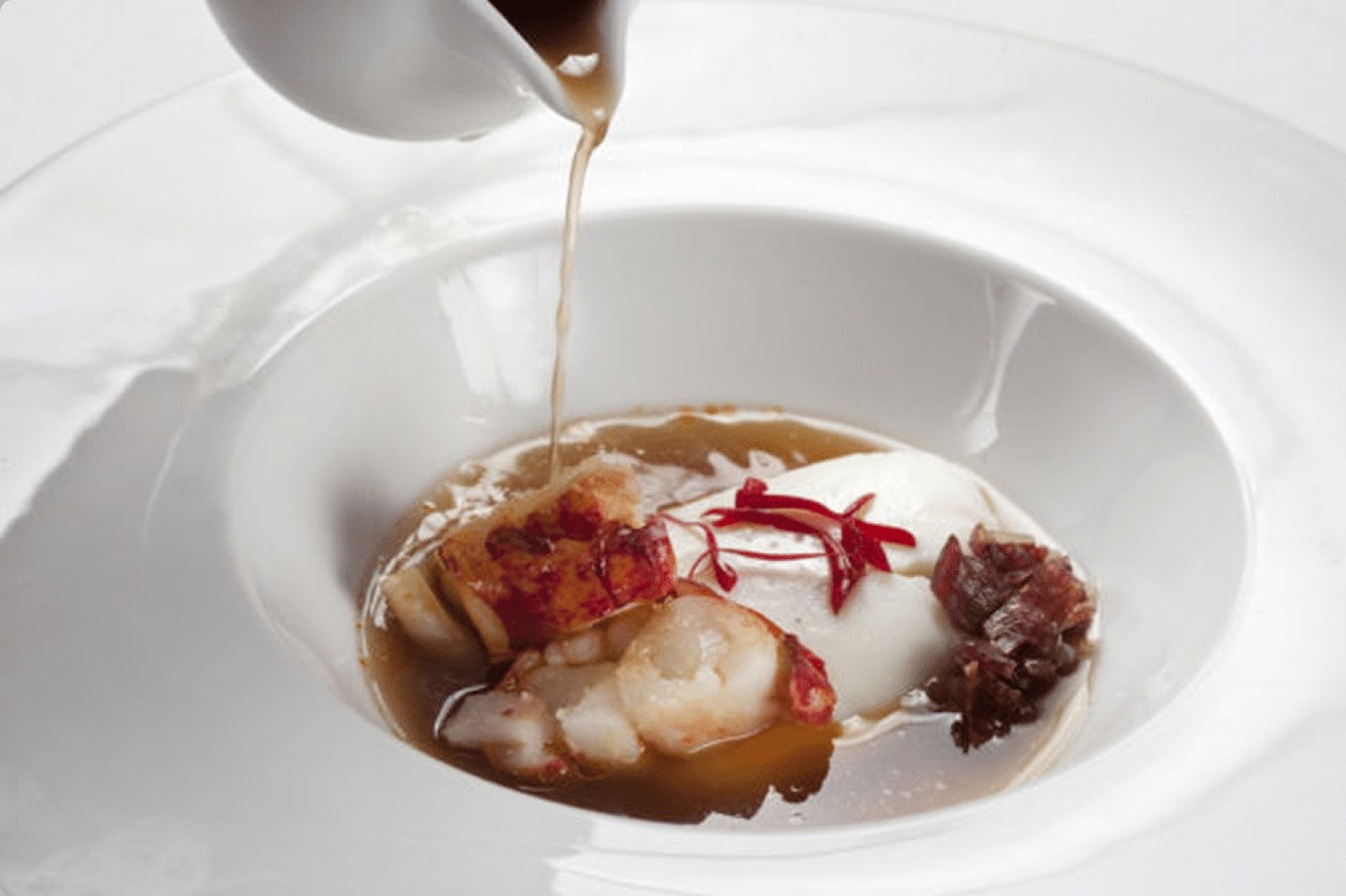 Consommé poured tableside over lobster and a white purée, with a dark relish garnish, at Nectari in Barcelona