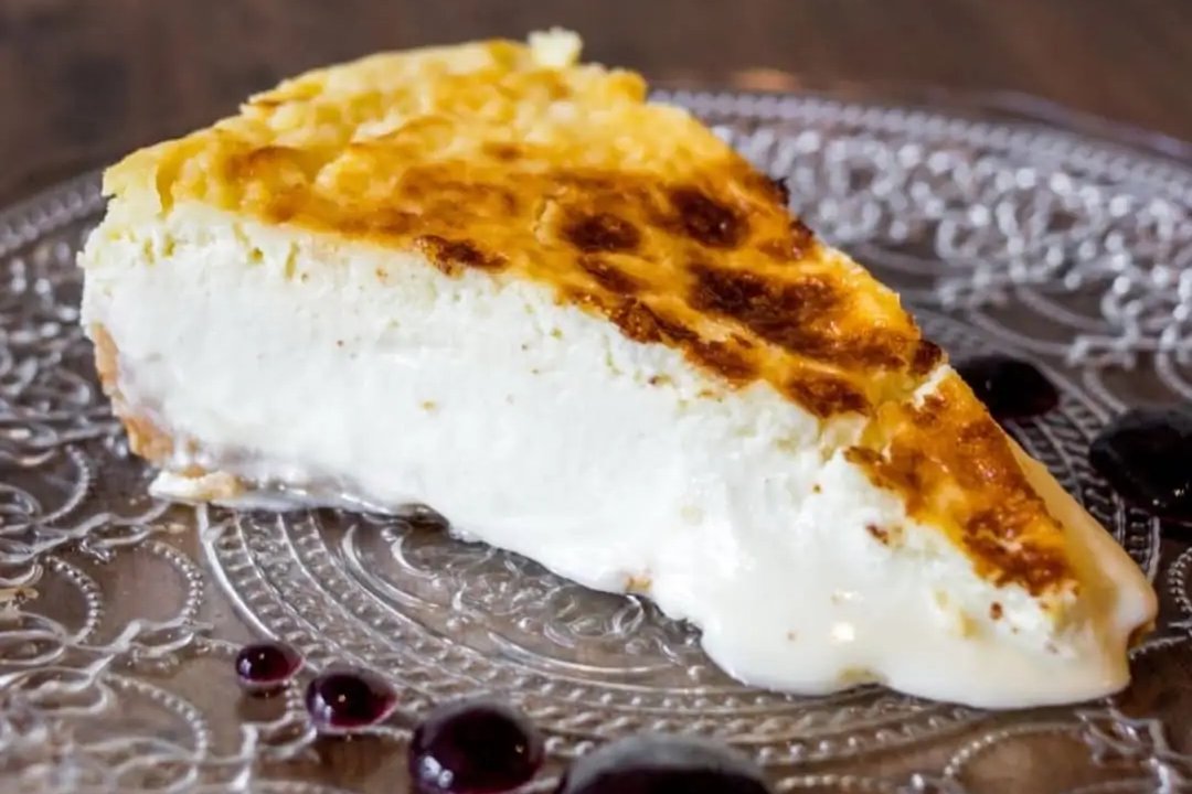 A slice of cheesecake with a caramelised top on a patterned glass plate with dots of dark berry sauce