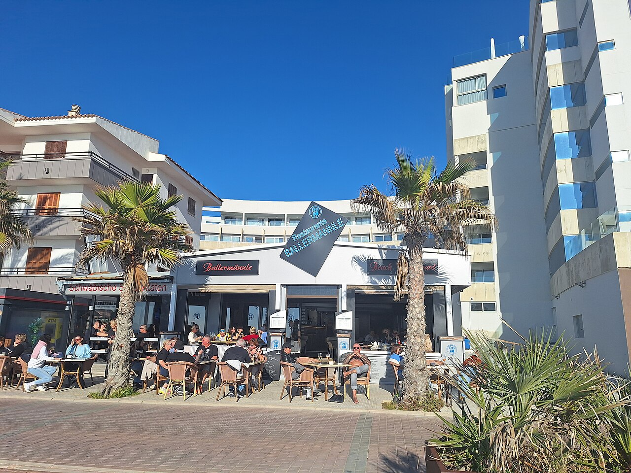 Diners sitting at outdoor tables in full sun on a beachfront restaurant terrace at Platja de Palma, Mallorca.