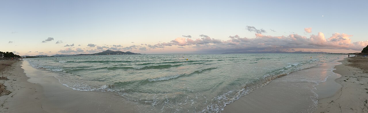 Panoramic view of Platja de Muro beach at sunset, with calm turquoise water and pastel clouds